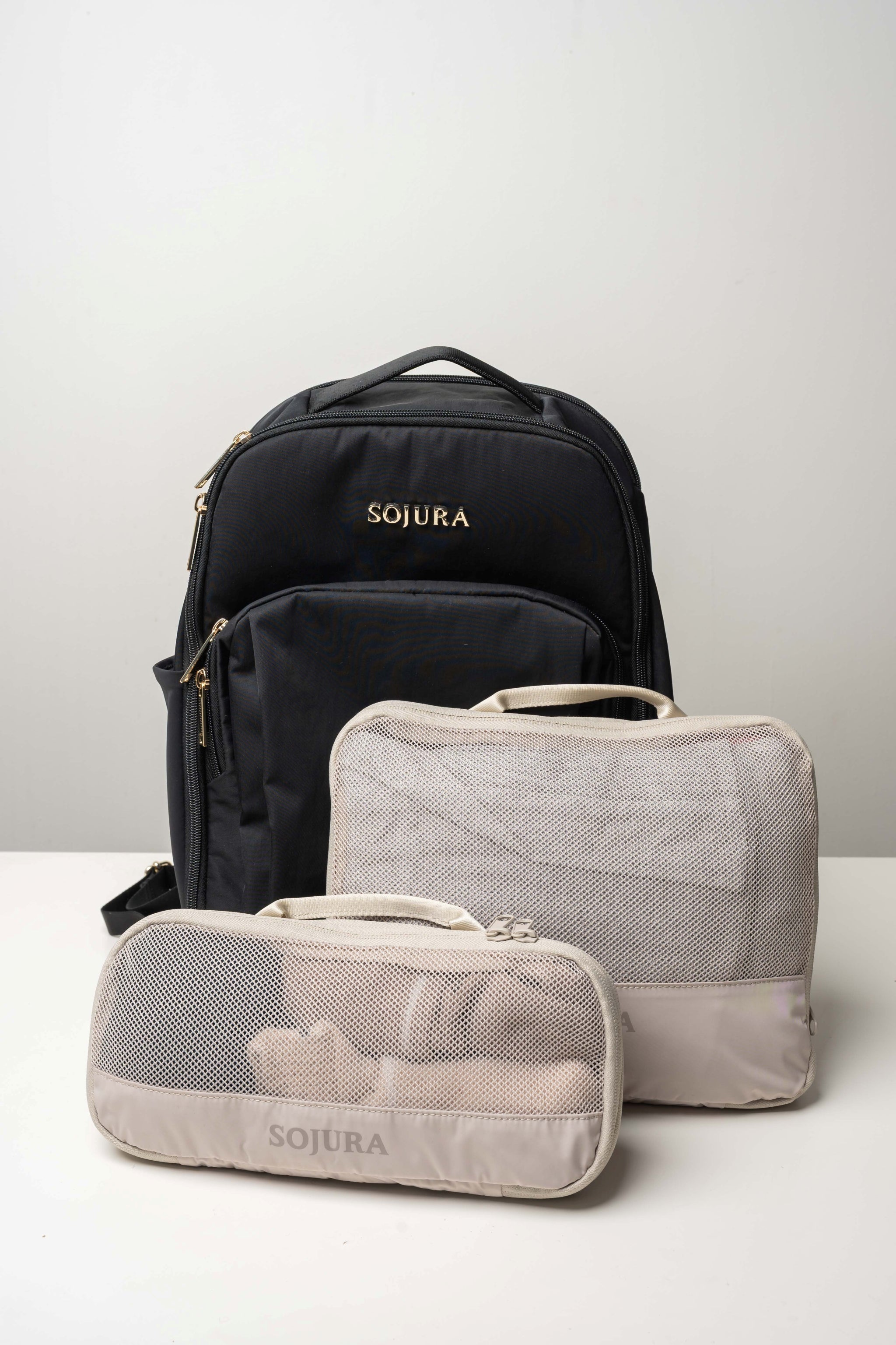 medium and small packed sojura compression packing cubes standing against a black sojura adella womens travel backpack