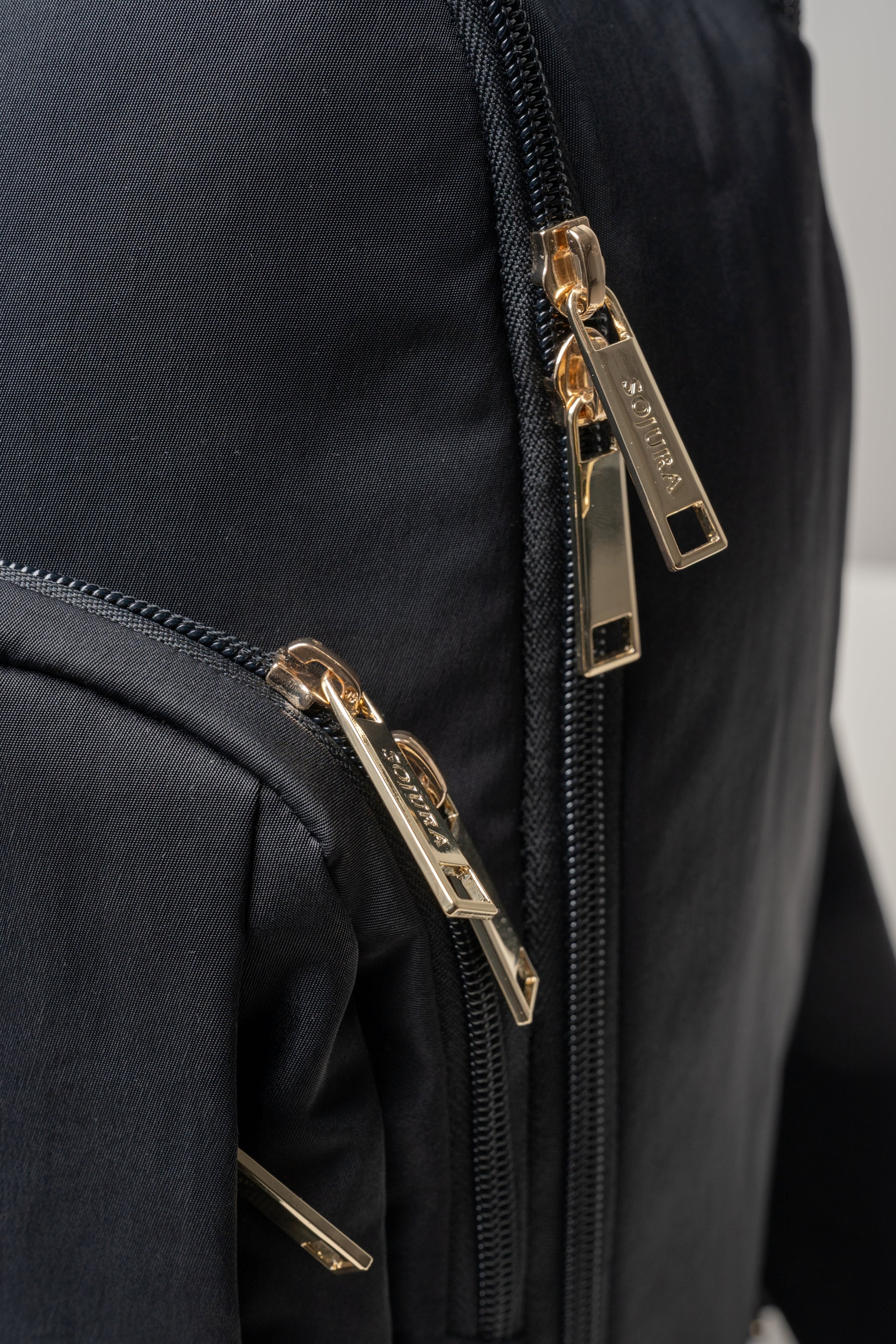 Light gold Sojura zippers on black travel backpack